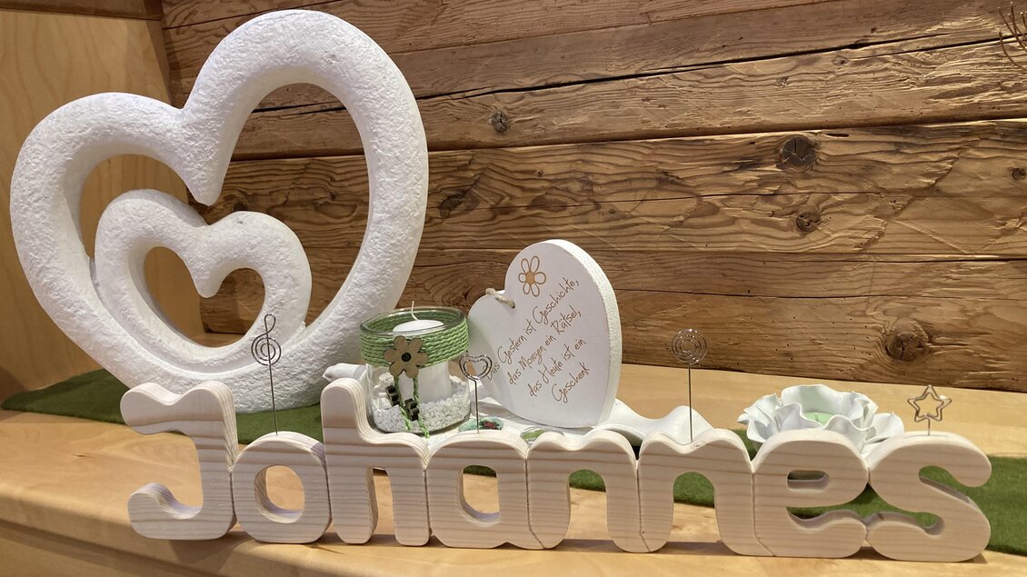 Ein hübsches Arrangement mit einer herzförmigen Dekoration und dem Namen „Johannes“ aus Holz. Dazu gehören auch ein kleiner Glasbehälter und eine beschriftete Herzform. | © Christian Stocker