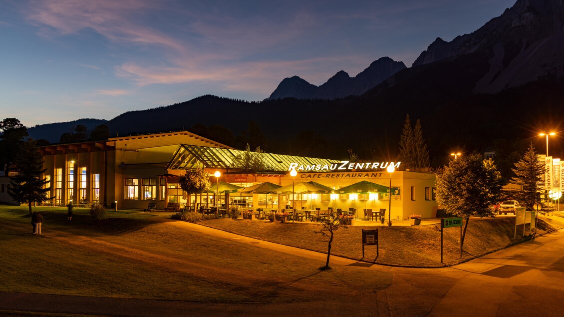 Ein gemütliches Café-Restaurant mit erleuchtetem Außenbereich inmitten einer malerischen Berglandschaft. Die Umgebung ist mit Bäumen und sanften Hügeln geschmückt. | © Hans-Peter Steiner