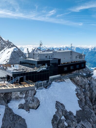 A modern building on a snow-covered mountain peak. In the background, a majestic mountain landscape stretches out under a clear blue sky. | © Josh Absenger
