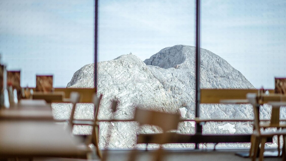 Ein Blick aus einem modernen Restaurant auf einen imposanten Berg. Die Tische sind sauber und minimalistisch eingerichtet, während der Berg im Hintergrund majestätisch hervorsticht. | © Christoph Huber