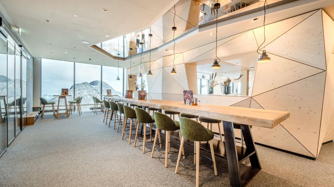 Ein modernes Café mit einer langen Holzbar und eleganten Stühlen. Große Fenster bieten einen Blick auf eine schöne Landschaft. | © Christoph Huber