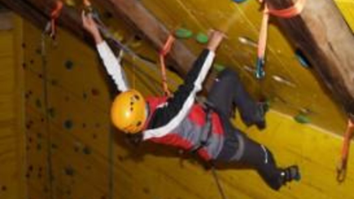 Ein Kletterer übt in einer Kletterhalle an einer gelben Wand. Der Sportler trägt einen Helm und Sicherheitsausrüstung. | © Martin Seebacher