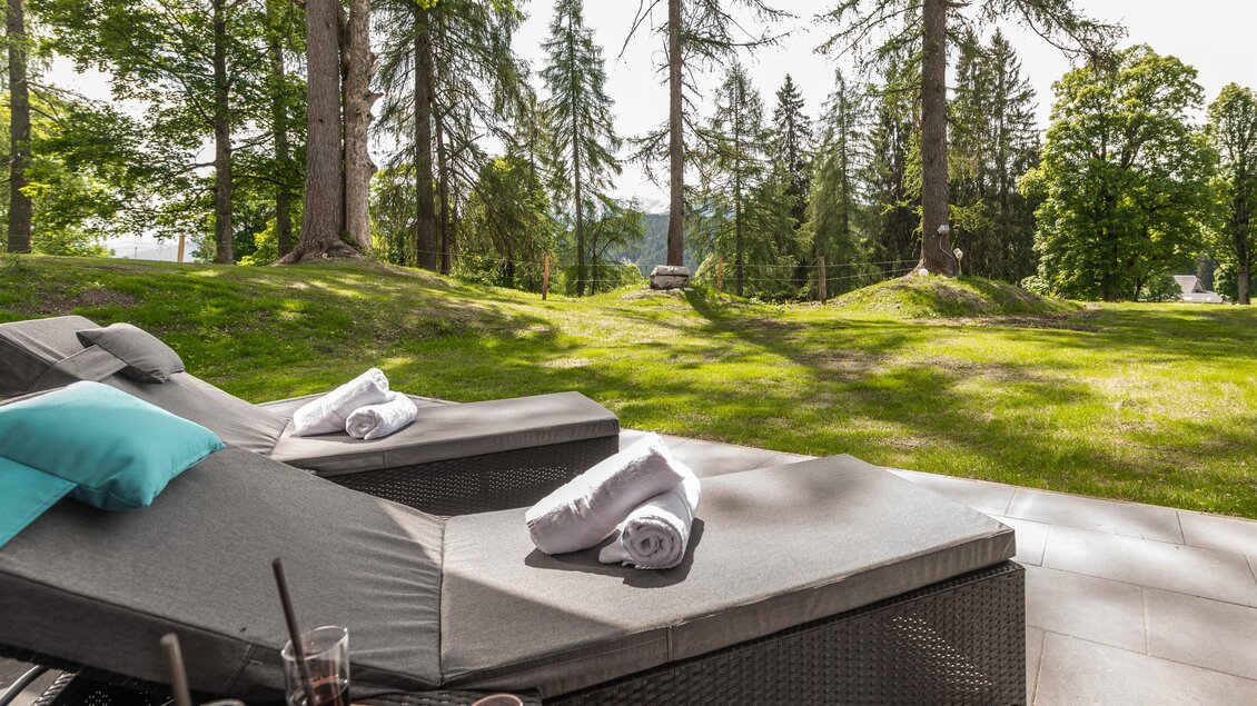 Eine entspannende Liegefläche im Freien mit Handtüchern und Getränken. Die Umgebung ist von hohen Bäumen und grünem Gras umgeben. | © Rösslhof