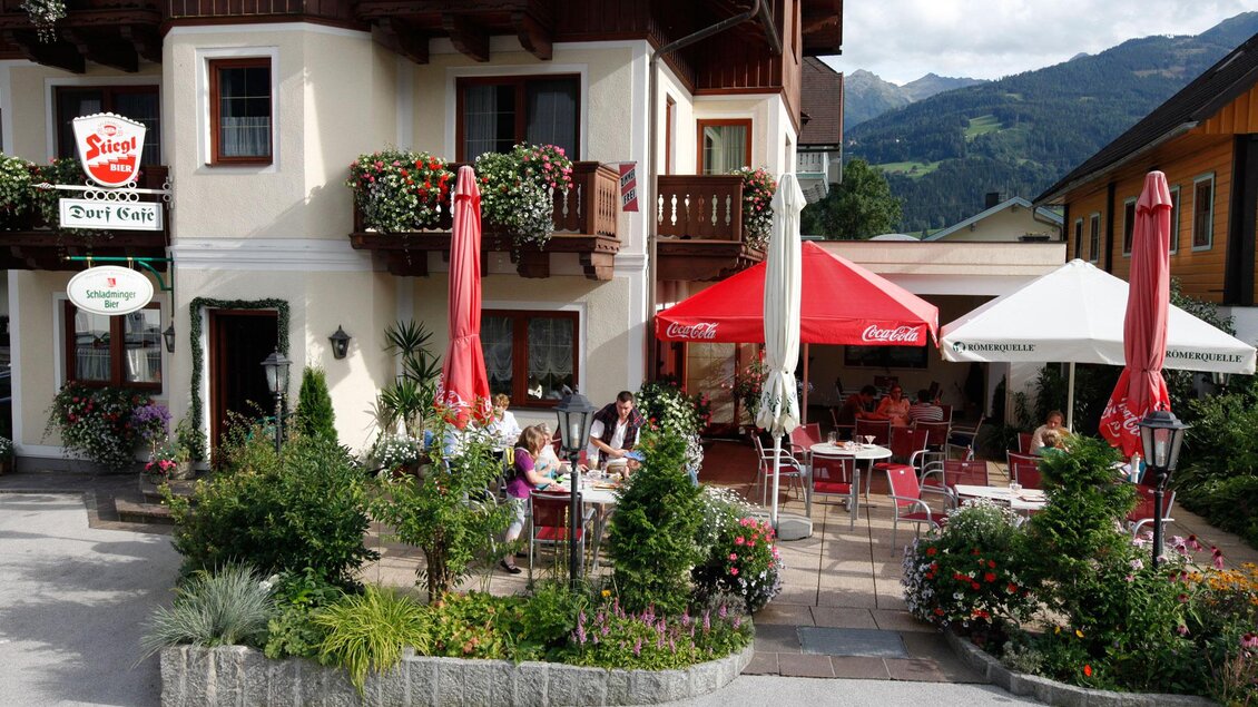 Ein gemütliches Restaurant mit Terrassen und bunten Sonnenschirmen. Im Hintergrund sind grüne Berge und Blumen zu sehen. | © Dorf Café