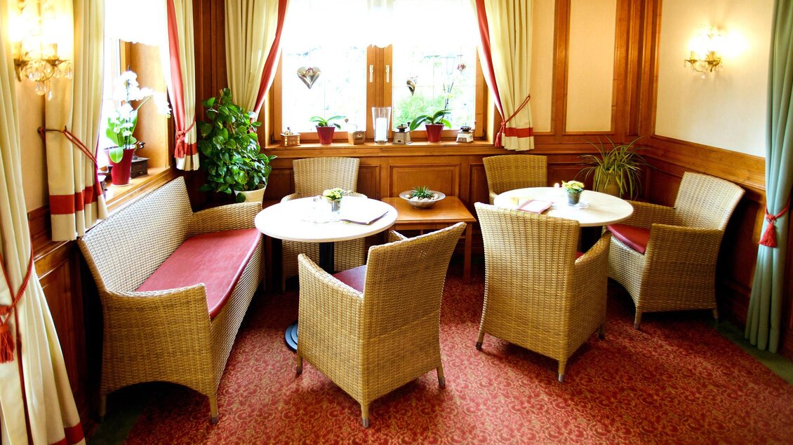 Ein gemütlicher Raum mit rattan Möbeln und einem runden Tisch. Große Fenster sorgen für viel Tageslicht und eine angenehme Atmosphäre. | © Dorf Café