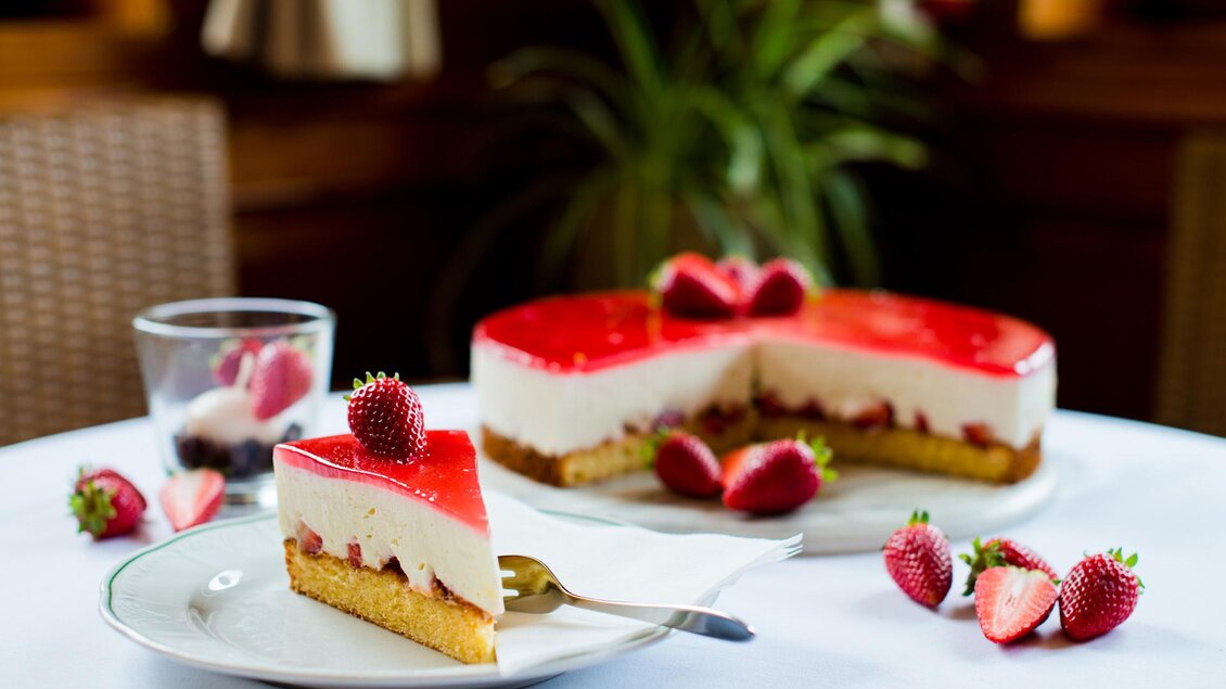 Ein köstlicher Erdbeerkuchen mit einer roten Geleeschicht. Umgeben von frischen Erdbeeren auf einem Tisch. | © Dorf Café