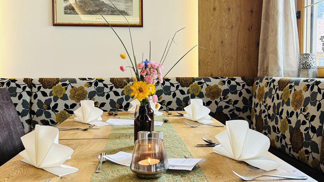 Ein einladender Tisch in einem Restaurant mit Holzoberfläche. Frische Blumen und stilvolle Servietten sorgen für eine gemütliche Atmosphäre. | © Anna Gasser