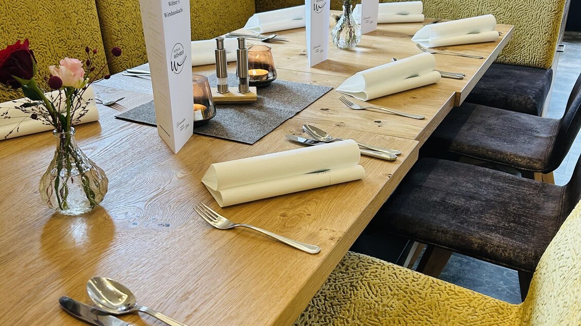 Ein modern gestalteter Tisch mit bunten Stühlen. Auf der Tischdecke liegen Besteck, Servietten und kleine Blumenvasen. | © Anna Gasser