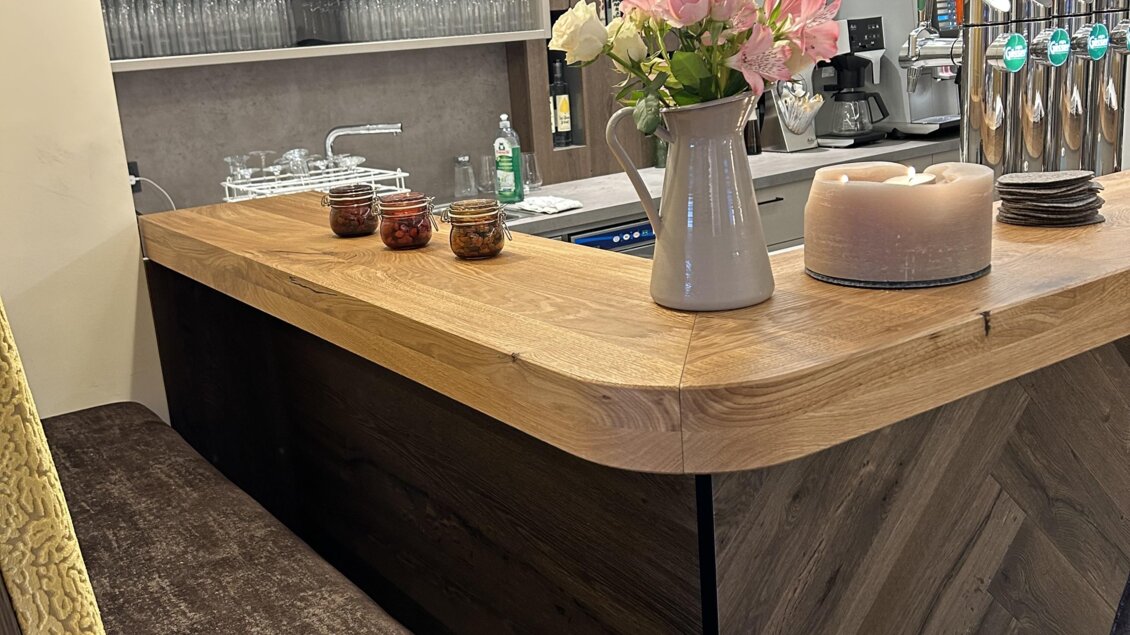 Eine stilvolle Bar mit einer Holztheke und modernen Hängelampen. Auf dem Tisch stehen frische Blumen und verschiedene Getränke. | © Anna Gasser