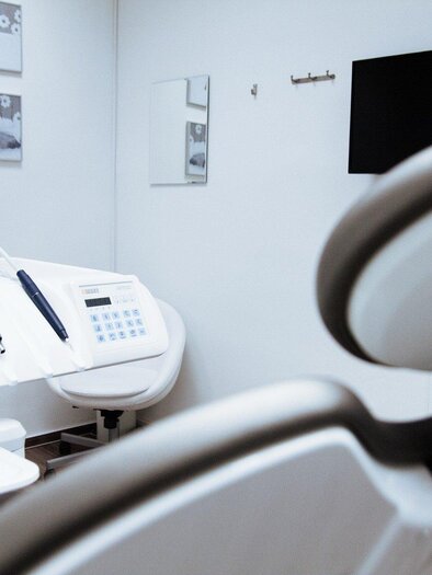 A bright dental chair in a modern treatment room. In the background, dental instruments and a television on the wall are visible.