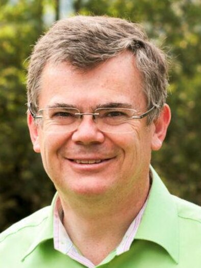 Ein lächelnder Mann mit Brille trägt ein grünes Hemd. Im Hintergrund sind Bäume und ein verschwommener Garten zu sehen. | © Dr. Franz Ploder