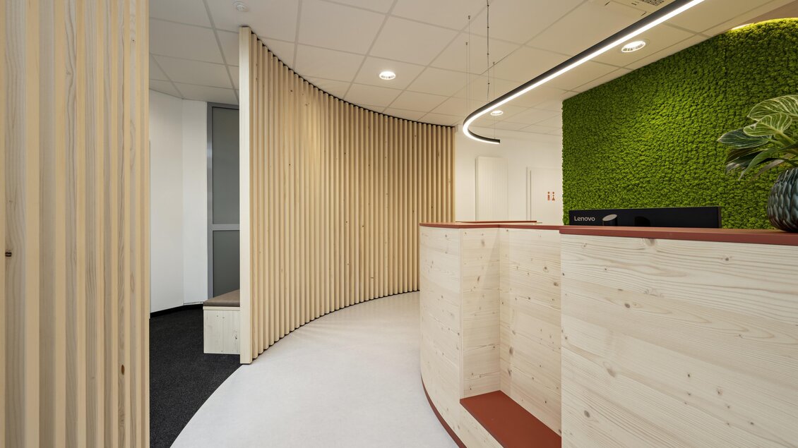 Ein moderner Empfangsbereich mit Holzverkleidungen und einer grünen Pflanzenwand. Der Raum ist hell und offen gestaltet, mit einem klaren, minimalistischen Design. | © Lorenz Masser