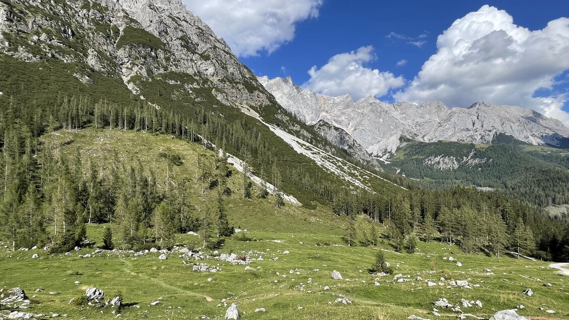 Eine idyllische Berglandschaft mit grünen Wiesen und hohen Felsen. Der Himmel ist blau mit einigen weißen Wolken. | © photo-austria.at/Hans-Peter Steiner