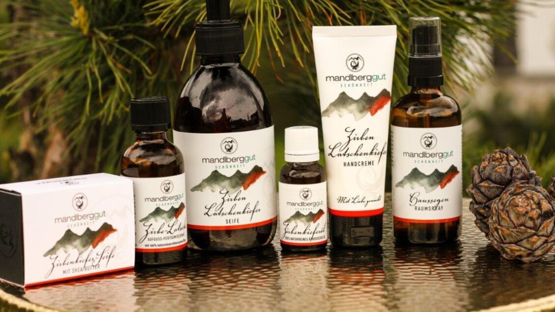 Verschiedene Naturkosmetikprodukte sind auf einem goldenen Teller präsentiert. Rundherum liegen als Deko Tannenzweige und -zapfen. | © Gerti Eder