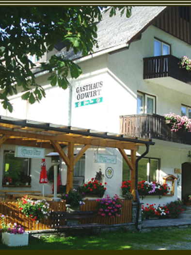 Das Bild zeigt ein tradtitionelles Gasthaus mit blumengeschmückten Balkonen und einer gemütlichen Terrasse - eine einladende Atmosphäre, die typisch für ländliche, alpine Regionen ist.
