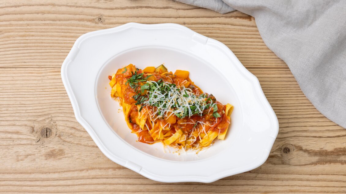 Ein Teller Pasta mit einer reichhaltigen Tomatensauce, garniert mit frischem Basilikum und Parmesan. Der Teller ist elegant auf einem Holzuntergrund platziert. | © ©Martin Huber