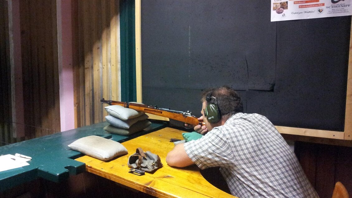 Ein Mann schießt am Schießstand mit einem Gewehr. Er trägt Ohrenschützer und hat sich an einer stabilen Ablage positioniert. | © Erzherzog-Johann-Schießstätte Aich