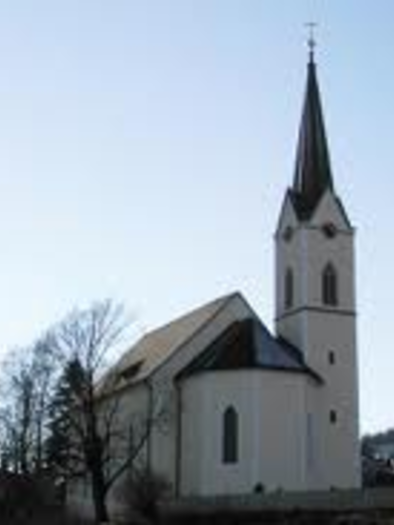 A white church with a tall tower stands against a clear blue sky. Surrounded by trees and hills, it showcases a peaceful rural scene. | © Evangelische Kirche Gröbming