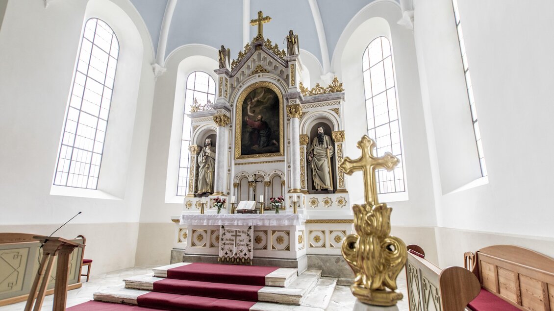 Eine helle Kirche mit einem prächtigen Altar und biblischen Statuen. Das Interieur ist schlicht, mit farbenfrohen Fenstern und einem roten Teppich. | © Gerhard Pilz