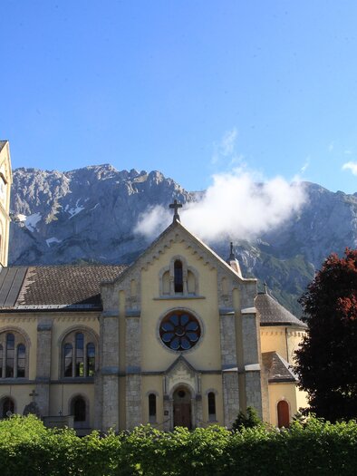 Pfarrkirche Ramsau am Dachstein vor beeindruckendem Bergpanorama und blauem Himmel. | © photo-austria/Hans Simonlehner