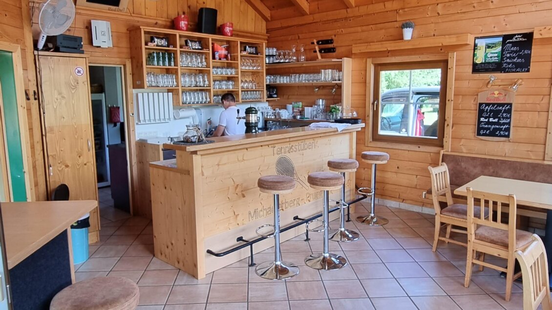 Ein gemütlicher Innenraum mit Holzdecke und Fliesenboden. Die Bar ist gut ausgestattet und es stehen Stühle und Tische bereit. | © FREI-ZEIT by Enns