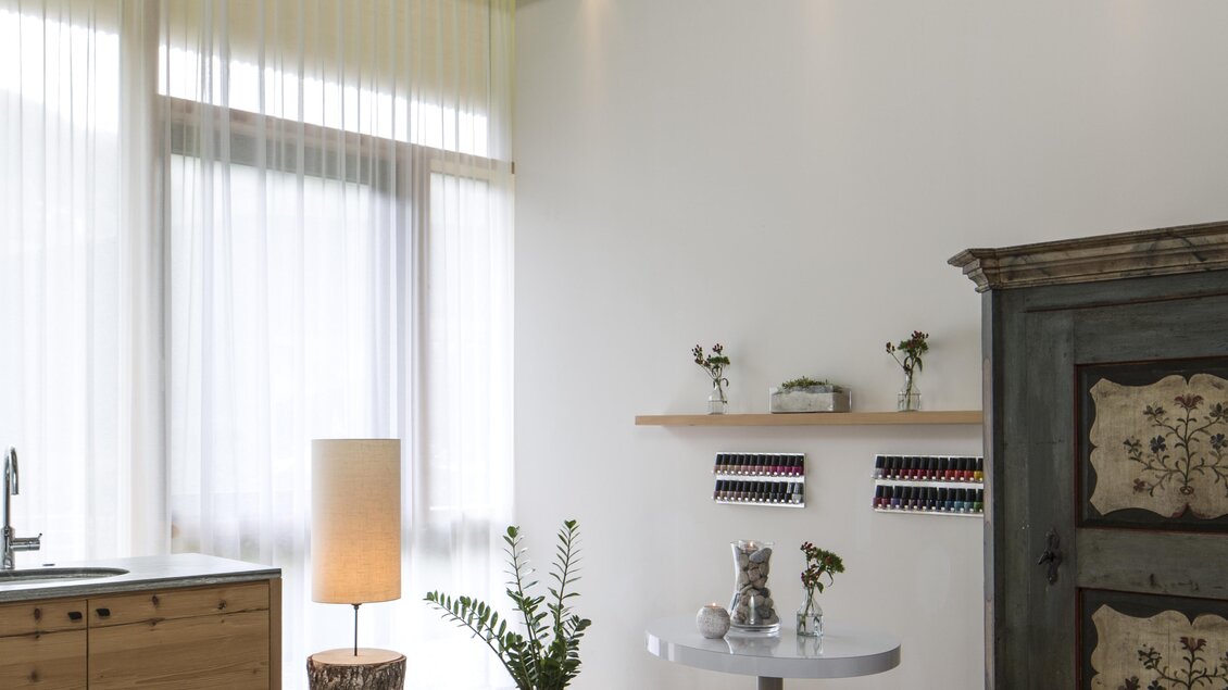 Ein entspannender Wellnessraum mit einem Massagetisch und großen Blumenbildern an der Decke. Helle Vorhänge und sanfte Möbel schaffen eine ruhige Atmosphäre. | © Falkensteiner Hotel Schladming/ Fotograf Walter Luttenberger