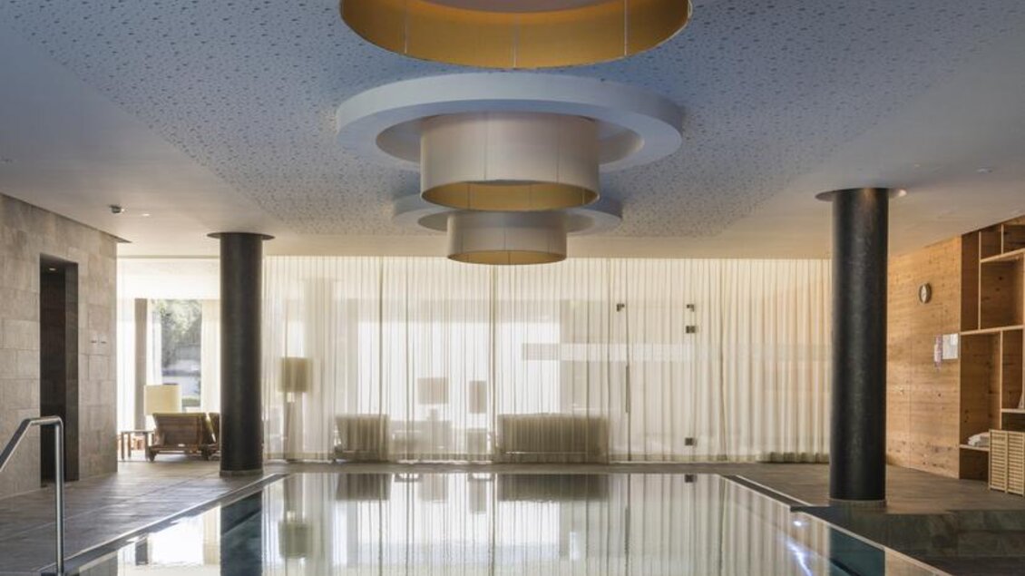 Ein eleganter Innenpool mit einem modernen Design und stilvollen Lampen. Die Umgebung ist hell und einladend, ideal zum Entspannen. | © Falkensteiner Hotel Schladming/ Fotograf Walter Luttenberger