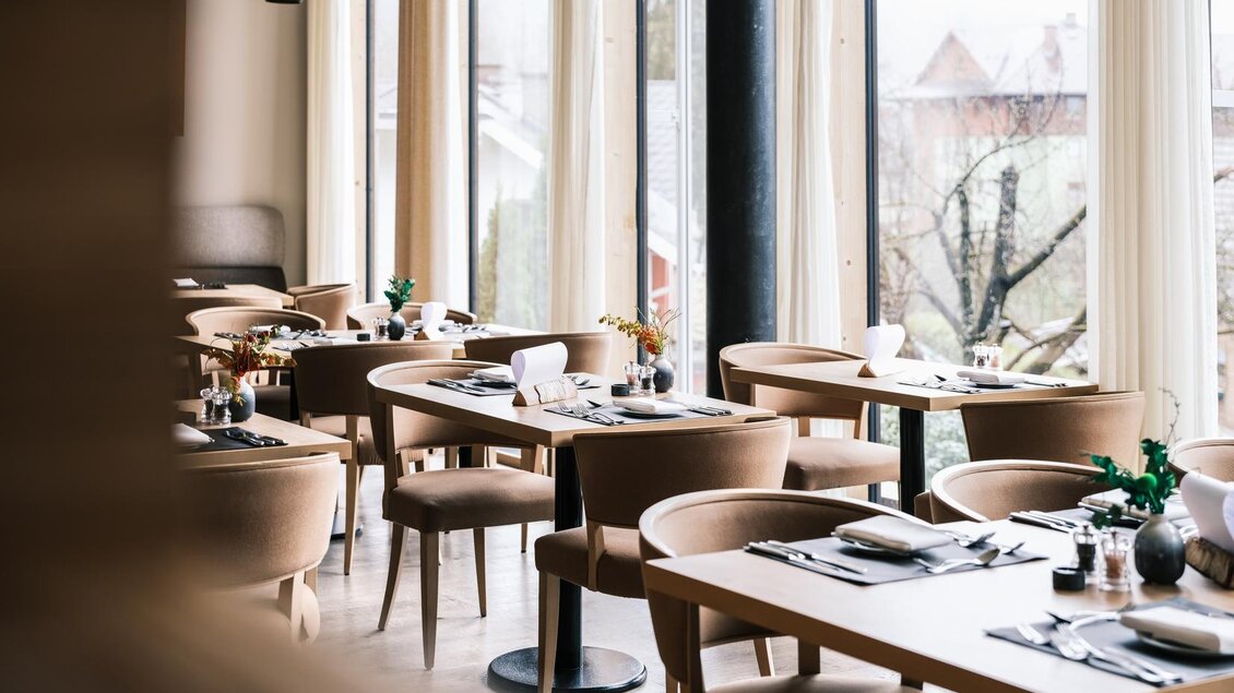 Ein stilvolles Restaurant mit gemütlichen Tischen und Stühlen. Große Fenster bieten einen Blick auf die Außenlandschaft. | © Falkensteiner Hotels &amp; Residences / Fotograf Dragan Dokmanovic