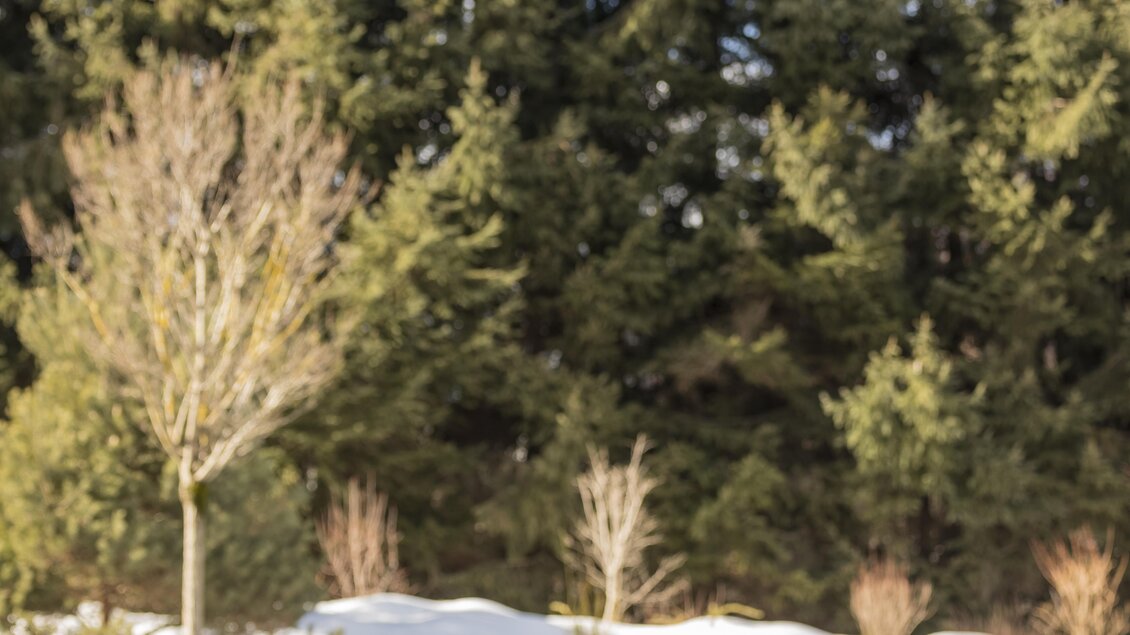 Ein Paar entspannt in einem Pool, umgeben von schneebedeckten Landschaften. Im Hintergrund sind hohe, grüne Bäume zu sehen. | © Falkensteiner Hotel Schladming/ Fotograf Walter Luttenberger