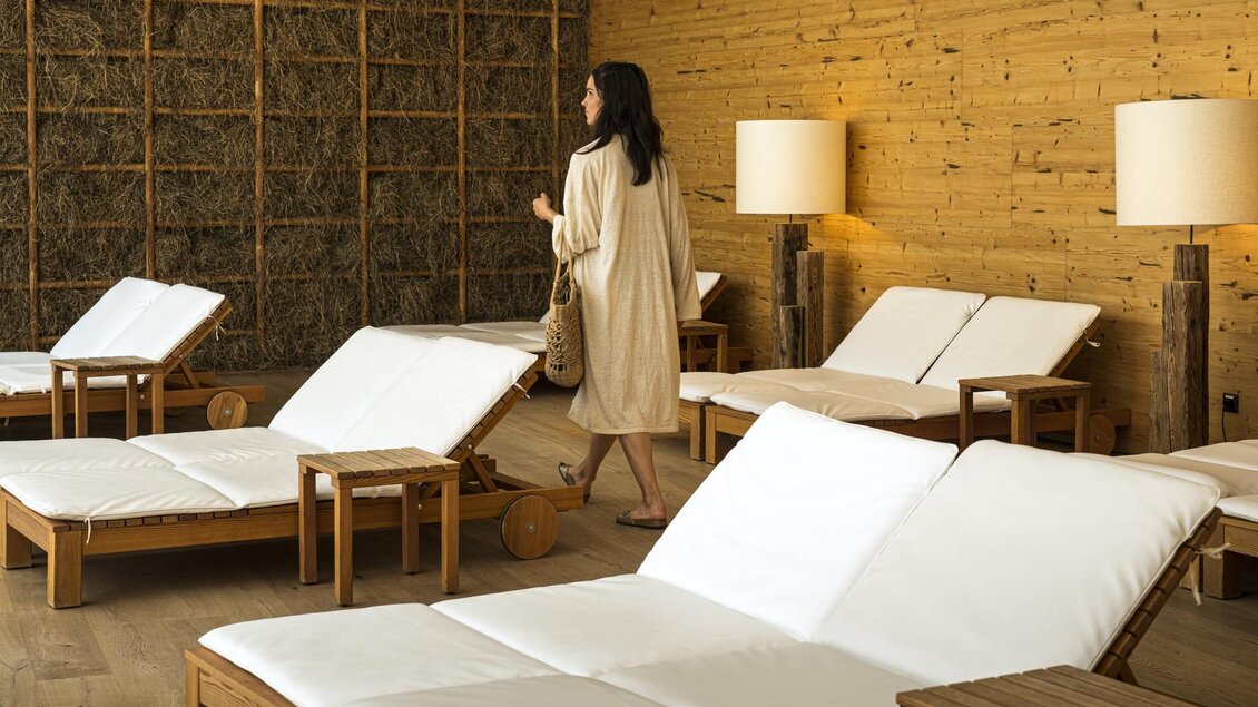 Ein ruhiger Wellnessbereich mit bequemen Liegen und warmen Holztönen. Eine Frau schlendert entspannt durch den Raum. | © Falkensteiner Hotel Schladming/ Fotograf Walter Luttenberger