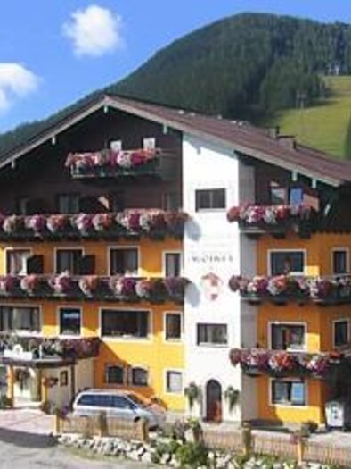 A charming hotel in the mountains, surrounded by green forests. The facade is colorful and decorated with many flowers. | © Familienhotel Austria