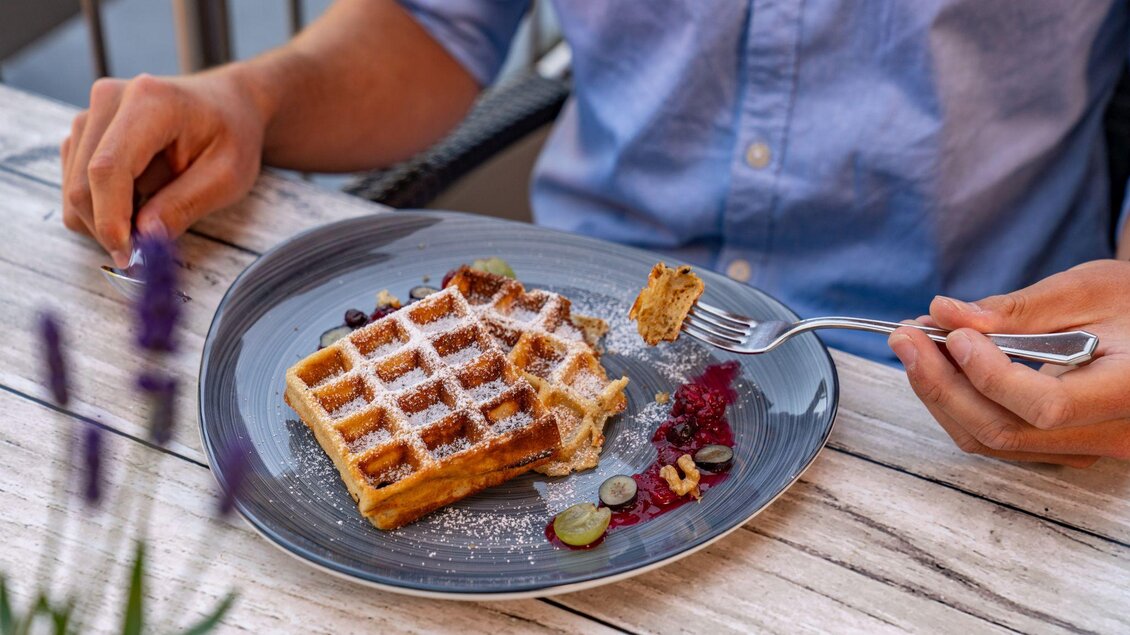 Eine Person, die gerade eine Waffel mit Marmelade und Staubzucker isst. | © Christine Höflehner