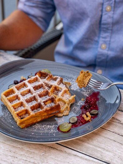 A person who is currently eating a waffle with jam and powdered sugar. | © Christine Höflehner