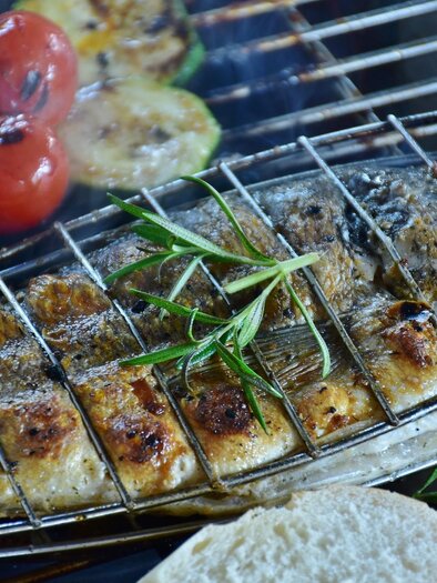 Gegrillter Fisch auf einem Rost mit frischem Gemüse. Im Hintergrund sind Tomaten und Zucchini zu sehen. | © Symbolfoto