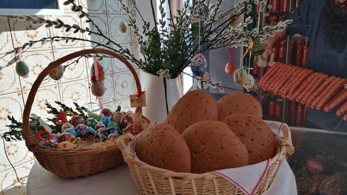 Ein schöner Tisch mit einem Korb voller bunter Ostereier und einem anderen Korb mit großen Lebkuchen. Es gibt auch dekorierte Zweige im Hintergrund. | © Fleischhauerei Tasch