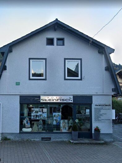 Ein graues Gebäude mit einem Schaufenster, in dem Fotos ausgestellt sind. Über dem Eingang ist der Schriftzug "Foto Steinfisch" zu sehen. | © Foto Steinfisch