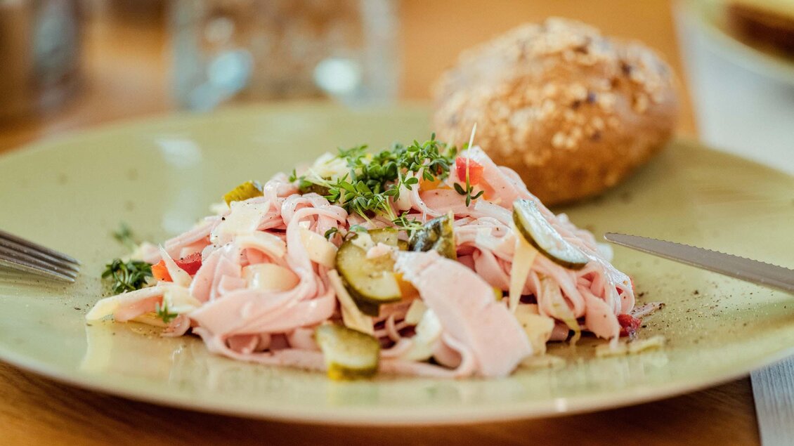 Ein Teller mit einem bunten Salat aus Schinken, Zwiebeln und Gurken. Dazu ein Brötchen aus Vollkorn. | © Stefan Trocha