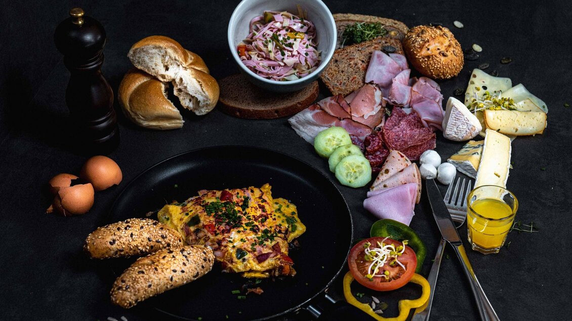 Ein köstliches Frühstück mit Rührei, Brötchen und einer Auswahl an Wurst und Käse. Dazu gibt es frisches Gemüse und ein Glas Saft. | © Stefan Trocha