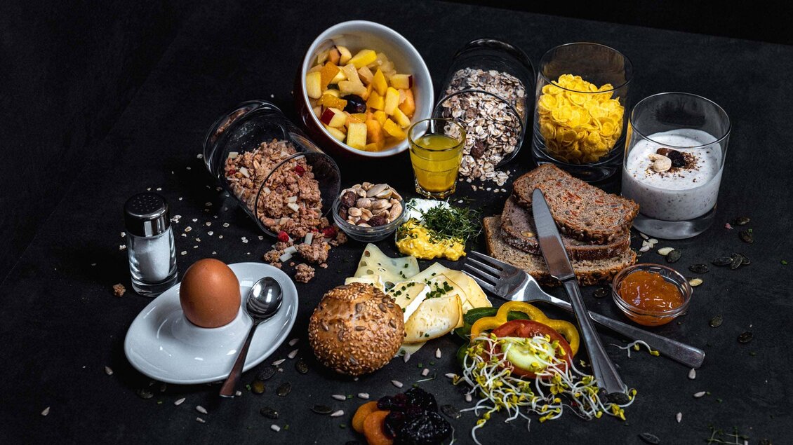 Ein liebevoll angerichtetes Frühstück mit verschiedenen Brötchen, Obst, Joghurt und Müsli. Die Auswahl umfasst auch ein gekochtes Ei und frisches Gemüse. | © Stefan Trocha