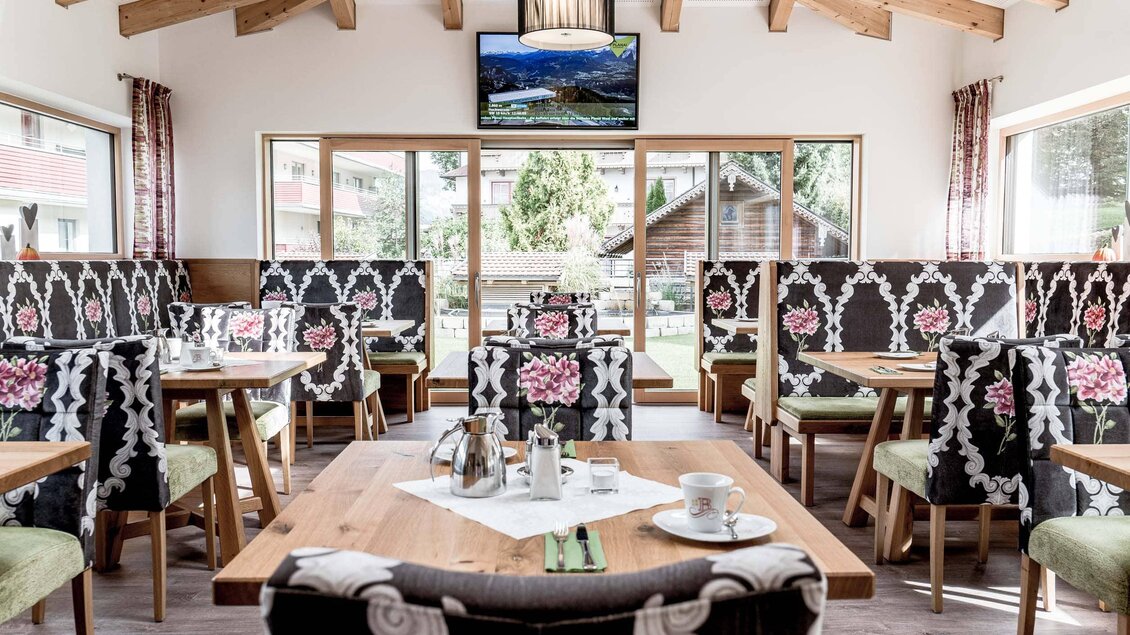 Ein einladendes Restaurant mit Holzbalkendecke und hellen Farben. Die Tische sind ordentlich gedeckt und die Wände sind mit stilvollen Blumenmustern dekoriert. | © Stefan Trocha