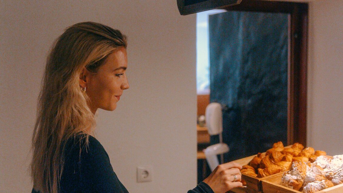 Eine Frau steht an einem Buffet mit frisch gebackenem Brot und Brötchen. Sie scheint zu überlegen, welches Gebäck sie wählen möchte. | © Stadthotel brunner