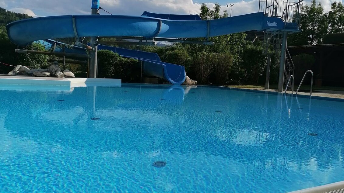Ein klarer Swimmingpool mit einer blauen Wasserrutsche. Im Hintergrund sind einige Bäume und ein blauer Himmel zu sehen. | © Gemeinde Mitterberg-Sankt Martin