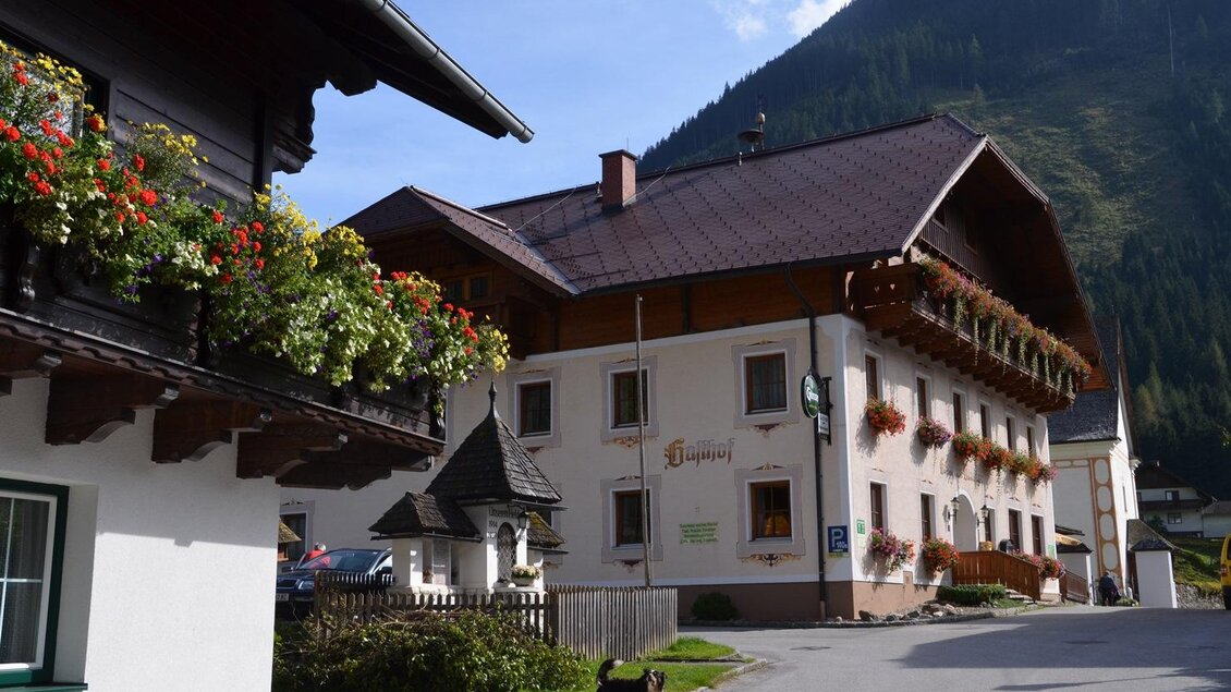 Ein malerisches Dorf mit traditionellen Häusern und bunten Blumen. Im Hintergrund sind grüne Berge und blauer Himmel sichtbar. | © Christian Tritscher