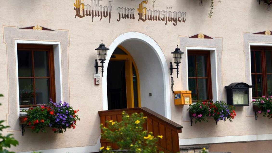 Ein charmantes Gebäude mit einem architektonischen Eingang. Über dem Eingang steht der Schriftzug "Gasthof zum Hammersjäger", umgeben von bunten Blumen. | © Christian Tritscher