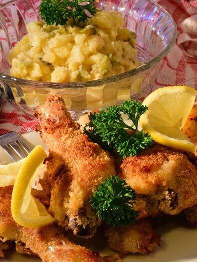 A plate with baked chicken, garnished with lemon slices and parsley. There is also a salad of potatoes in a bowl. | © Symbolfoto Pixabay