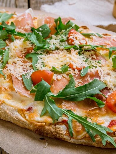 A freshly baked pizza with ham, arugula, and cherry tomatoes. The crust is crispy and golden brown. | © Gasthof Pinseria Kollerhof