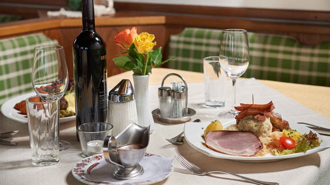 Ein schön gedeckter Tisch mit einem Gericht, bestehend aus Fleisch, Gemüse und Sauce. Auf dem Tisch stehen auch Wein, Wasser und Blumen. | © Gasthof Stockerwirt