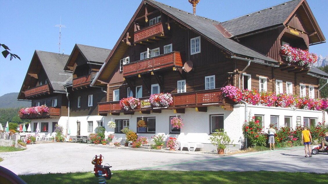 Ein charmantes Holzgebäude mit vielen Balconen, geschmückt mit bunten Blumen. Der umliegende Garten bietet einen schönen Platz zum Entspannen. | © Gasthof Stockerwirt