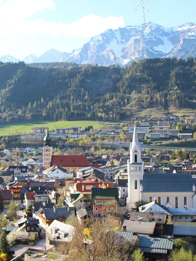 A picturesque town with colorful houses and a white church in the foreground. In the background, majestic mountains and a clear sky can be seen. | © Katrin Hutegger