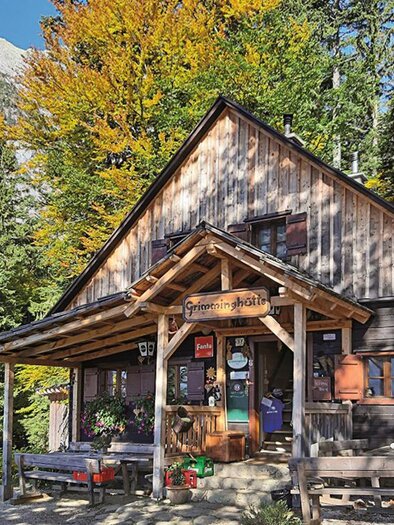 Eine malerische Hütte aus Holz, umgeben von buntem Herbstlaub. Die Holzveranda und die Bänke laden zum Entspannen ein. | © Grimminghütte